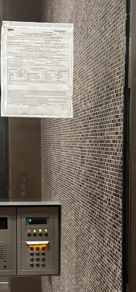 A city notice taped to the glass of a building vestibule, beside the intercom panel