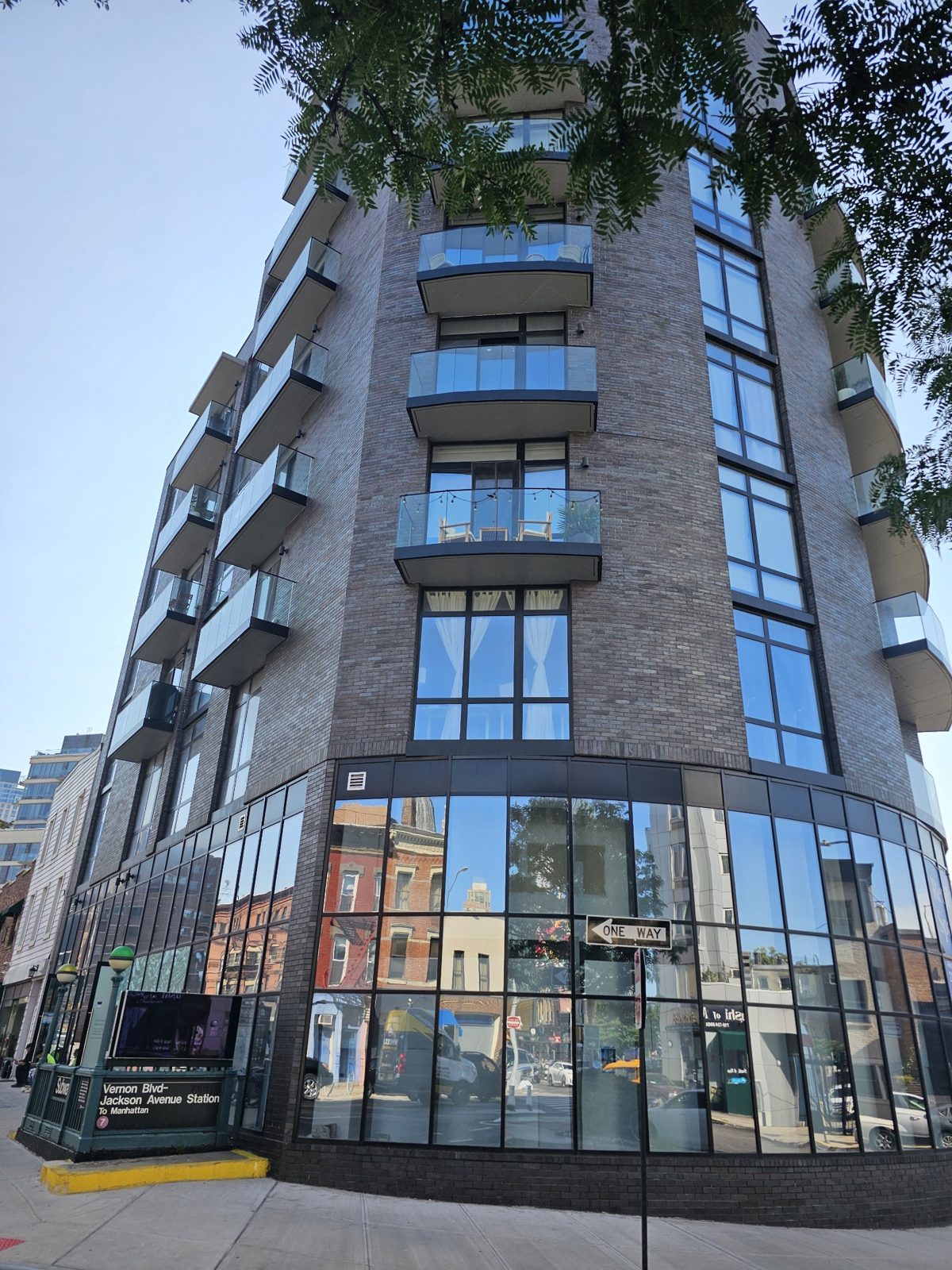 The curved ground-floor storefront of The Anable beside the Vernon Boulevard-Jackson Avenue subway entrance, with balconies above