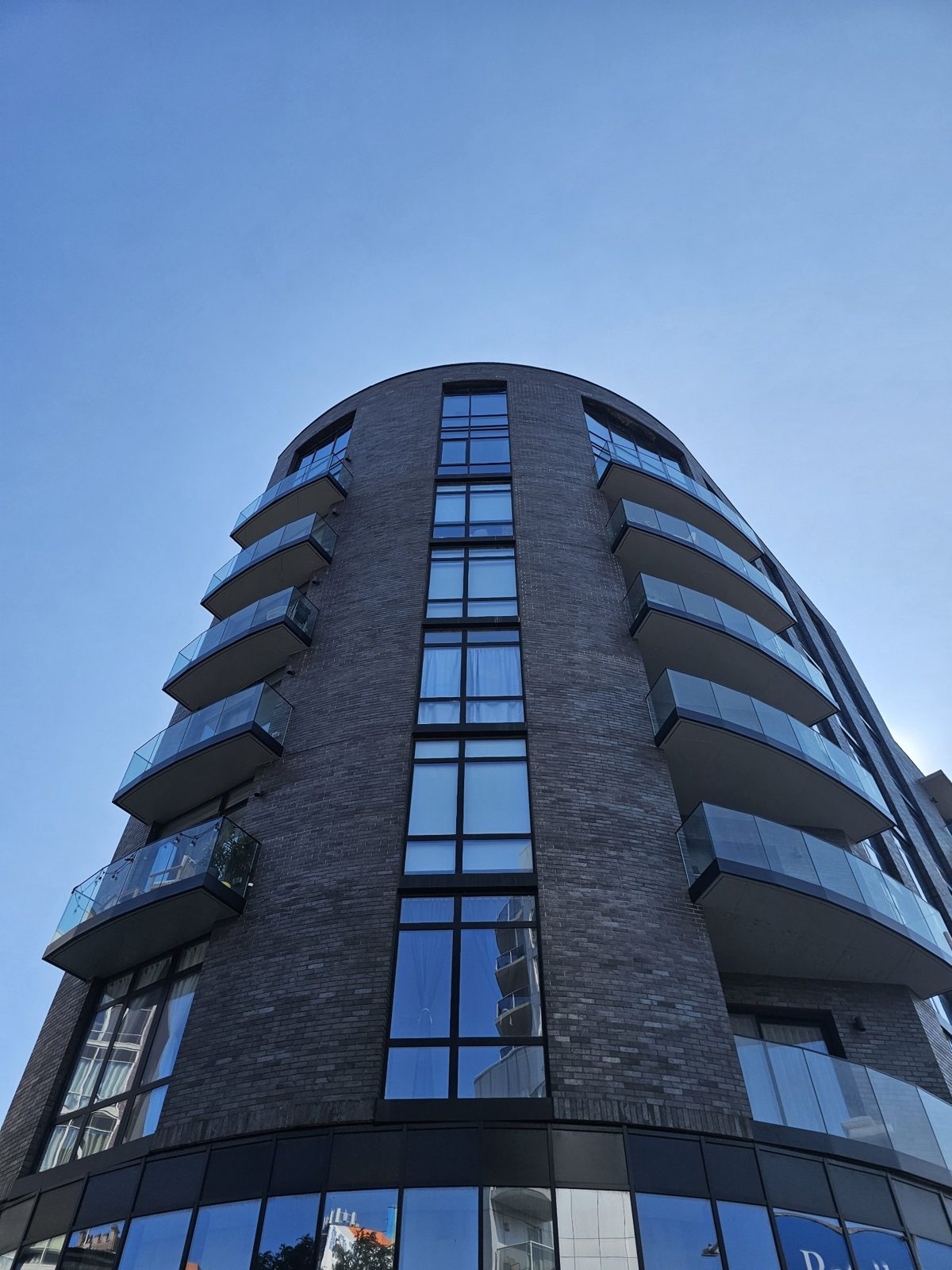 Looking up the curved corner of The Anable: a full-height column of windows between curved glass balconies