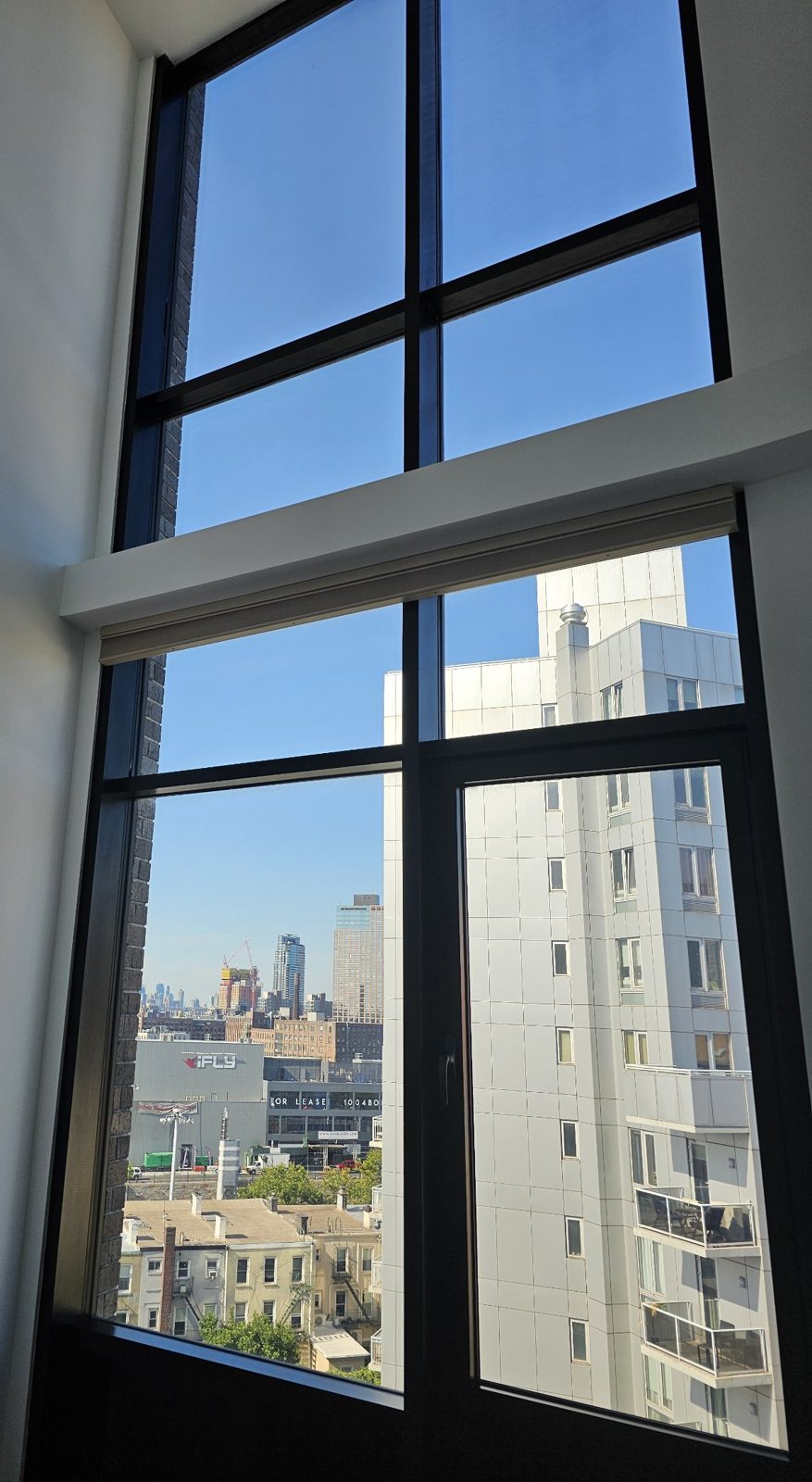 Inside an apartment at The Anable: a double-height wall of black-framed glass with an operable sash and a view over Long Island City