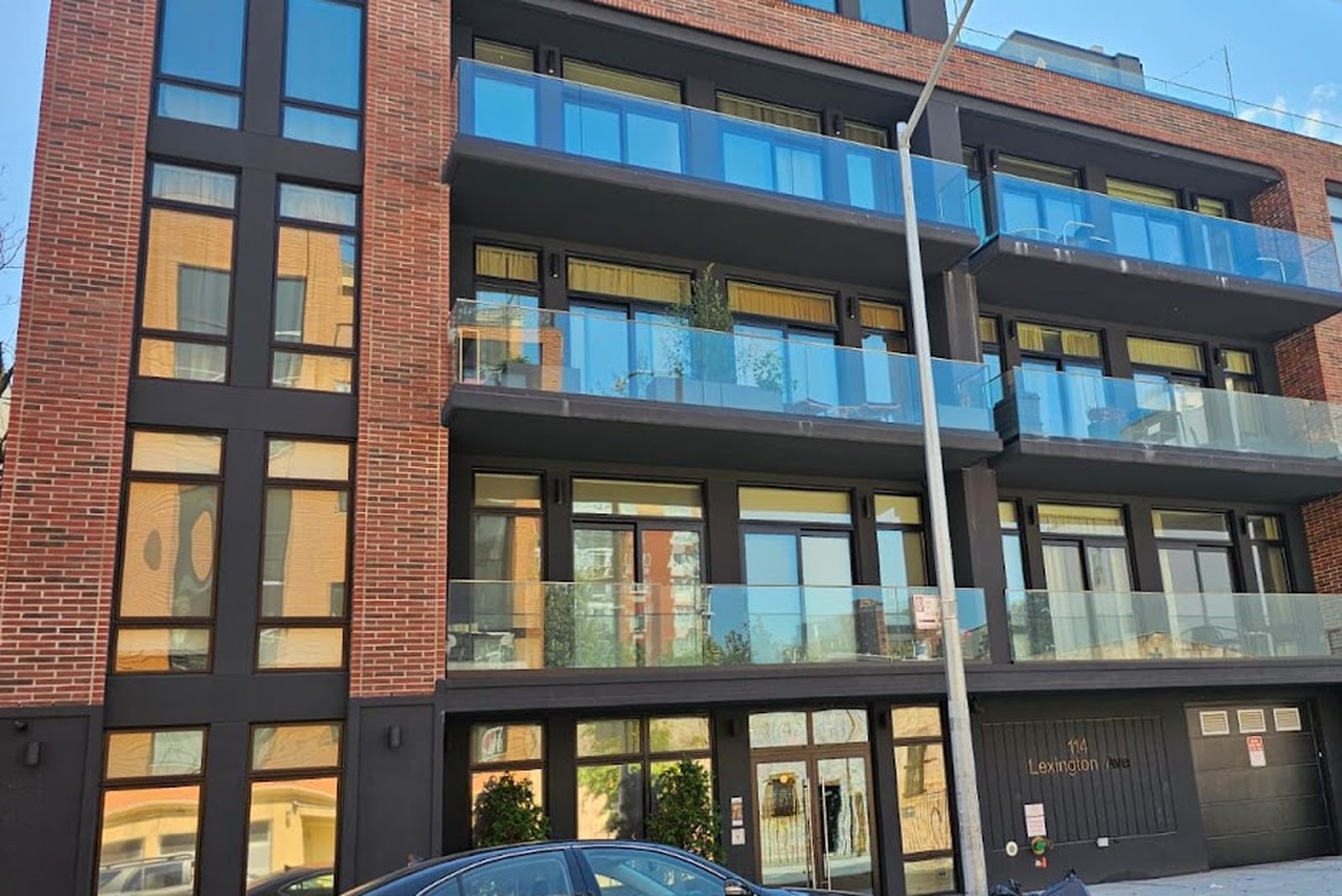 Glass balcony railings across the front of a new brick residential building at 114 Lexington Avenue, Brooklyn