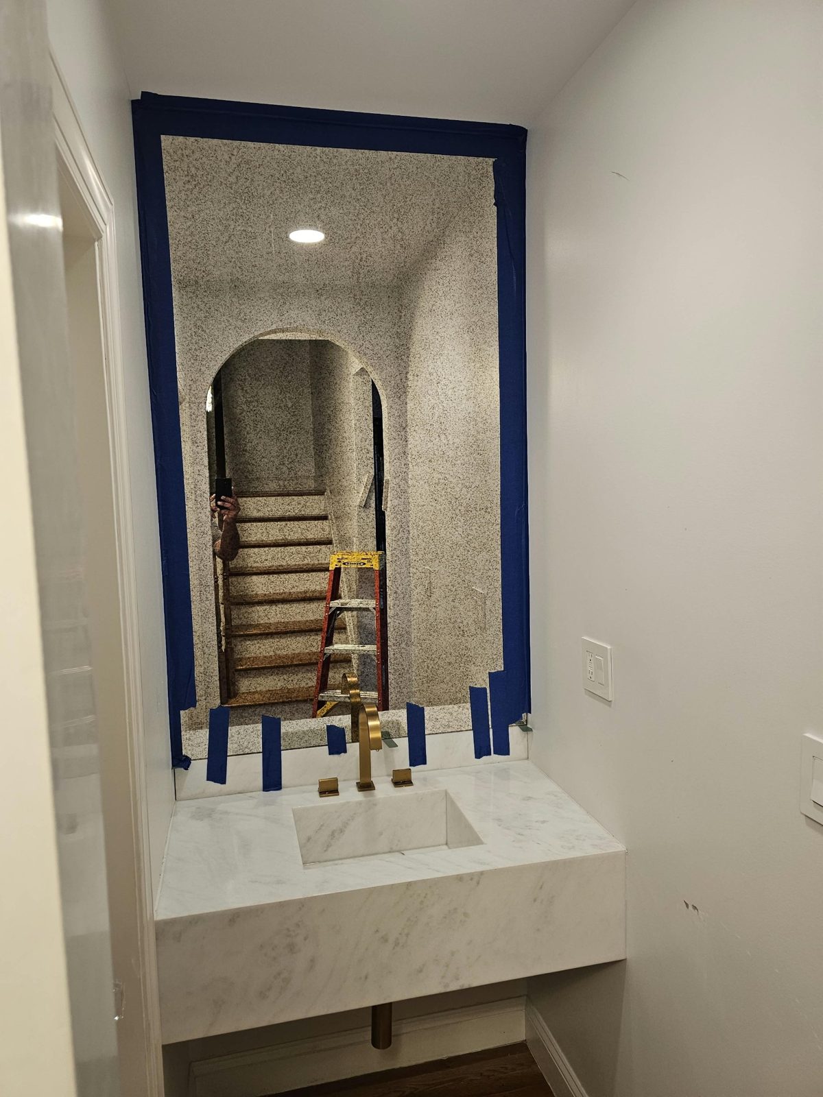 Speckled antique mirror fitted wall to wall above a floating white marble vanity with a brushed-gold faucet in a powder room in Borough Park, Brooklyn