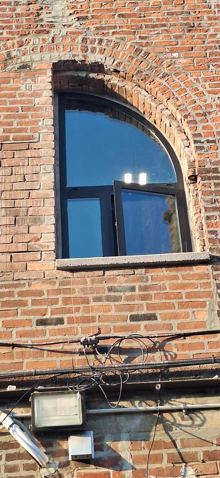 Custom half-arch black aluminium window with a quarter-round fixed top lite, a fixed lower lite and an open out-swing casement sash in a partly bricked-in arch at 185 Van Dyke Street, Red Hook