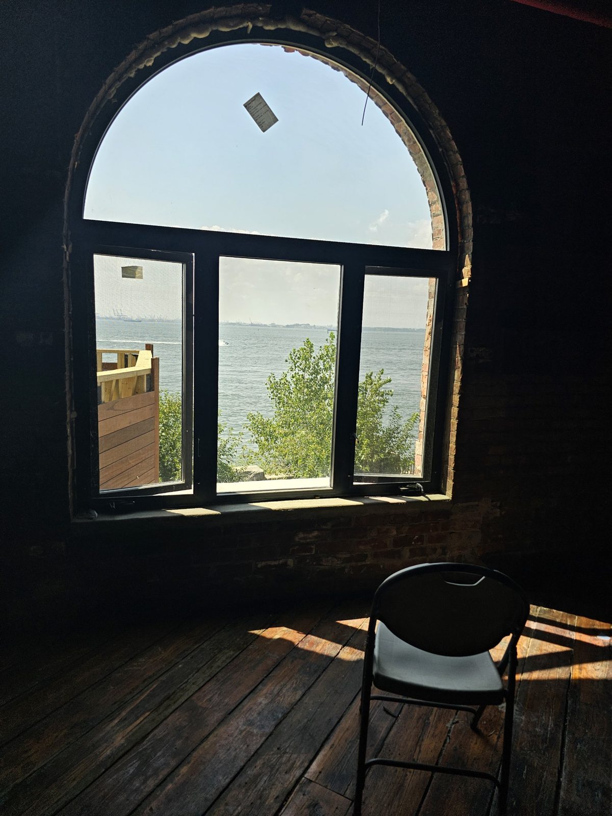 Interior view of a custom arched black aluminium window at 185 Van Dyke Street, Red Hook, with a fixed arched top lite, a fixed centre lite and two open out-swing casements with insect screens, looking out over New York Harbor