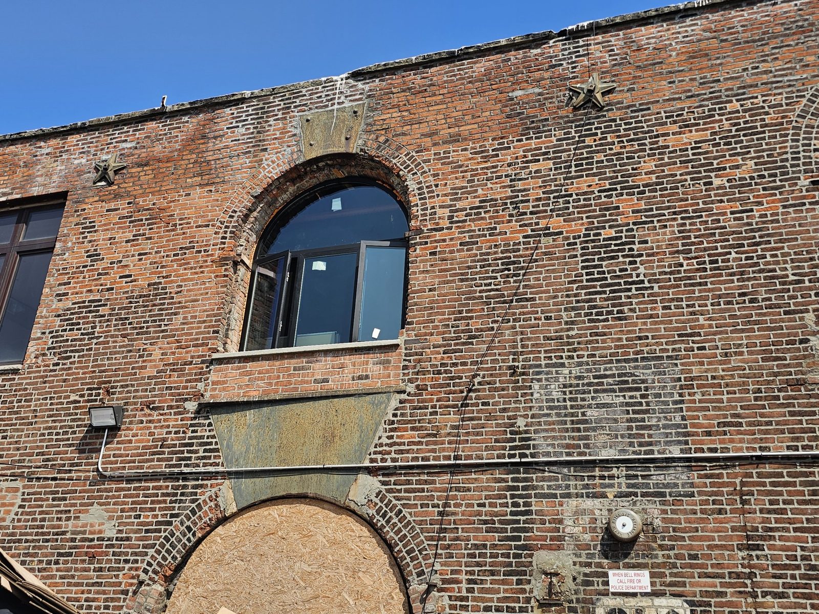 Arched black aluminum window with two out-swing casement sashes open, set in the brick facade at 185 Van Dyke Street, Red Hook, Brooklyn