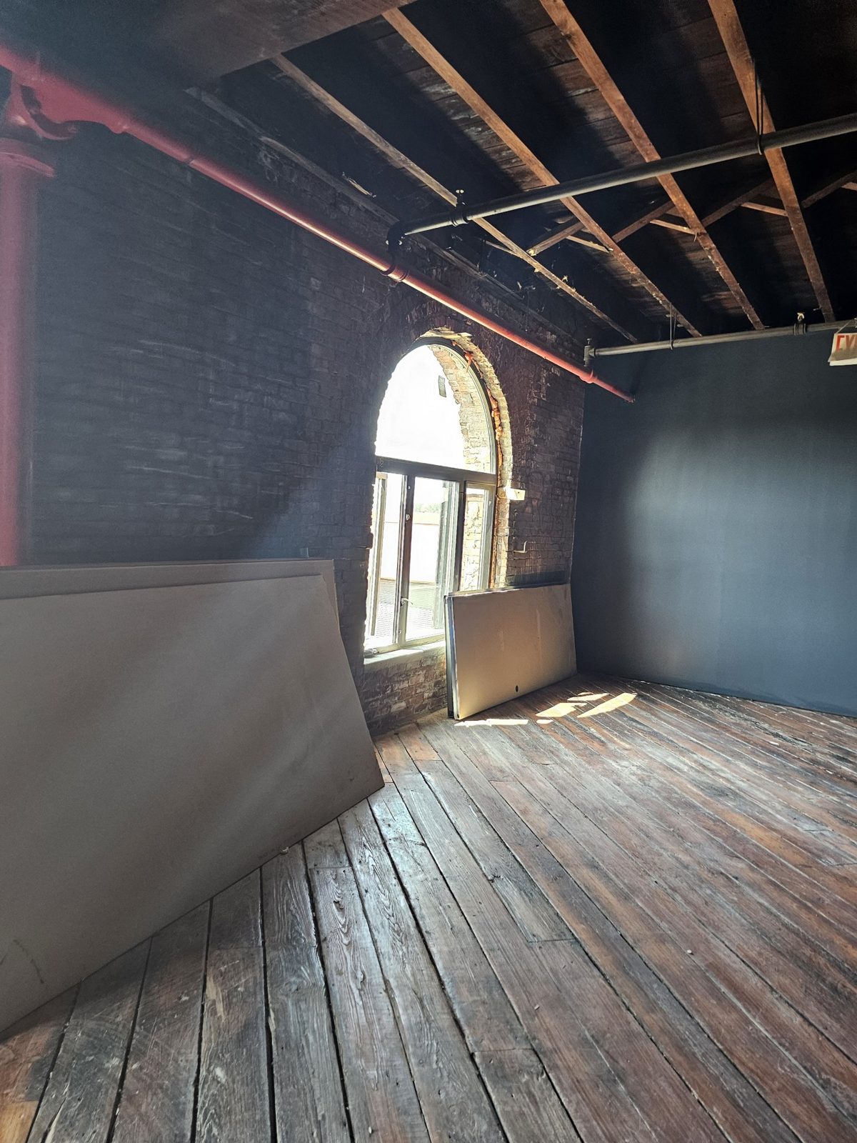 Interior view of an arched aluminum window in the brick wall of the warehouse at 185 Van Dyke Street, Red Hook, with timber joists and plank floor