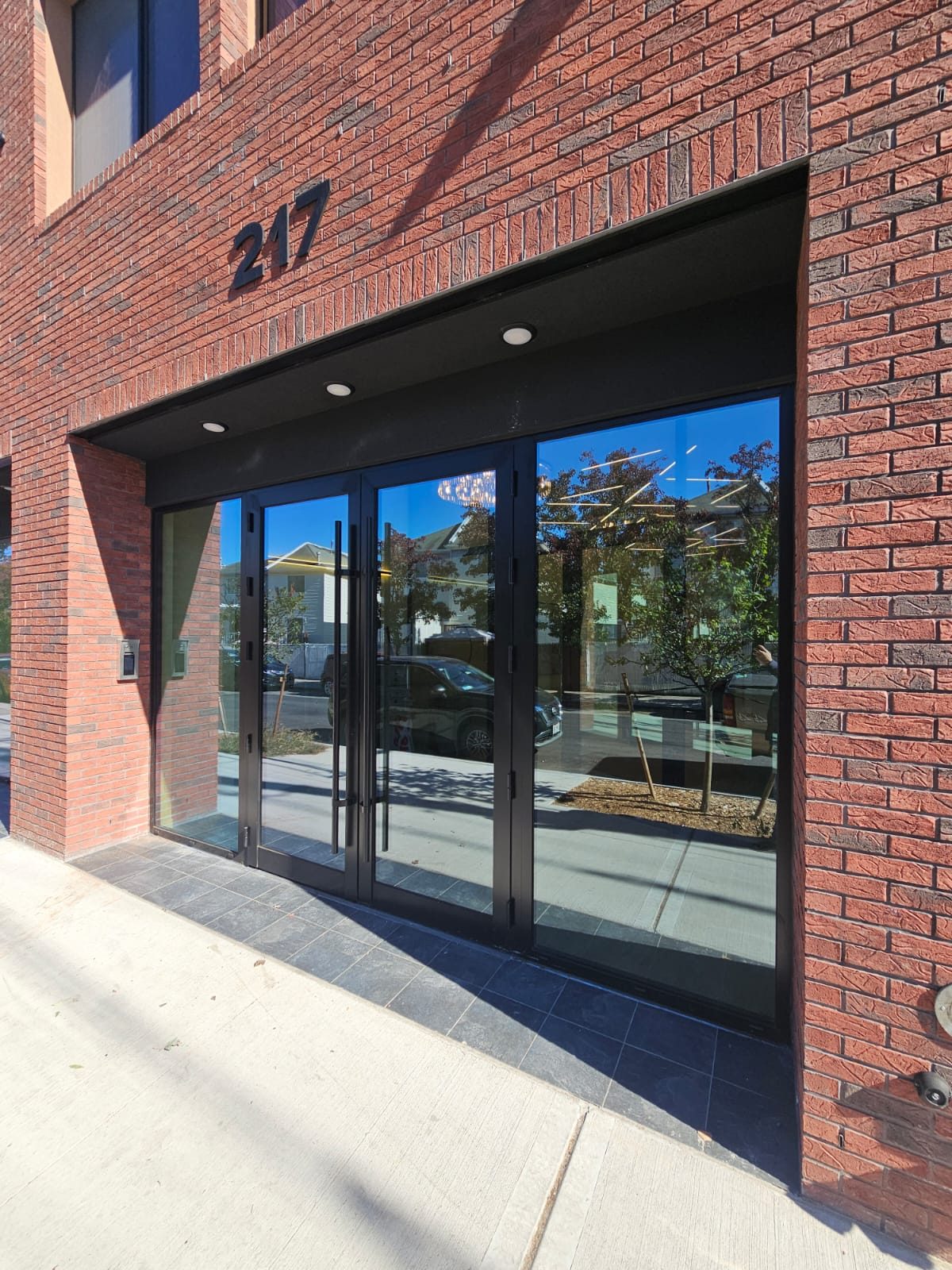Recessed brick entrance of 217 Main Street, Staten Island, with a pair of black aluminium glass doors, sidelites and full-height ladder pull handles
