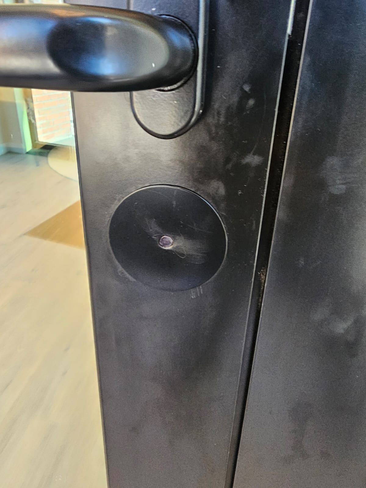 Black aluminium door stile at 217 Main Street, Staten Island, with a round cover patch closing the former lock cut-out below the lever handle