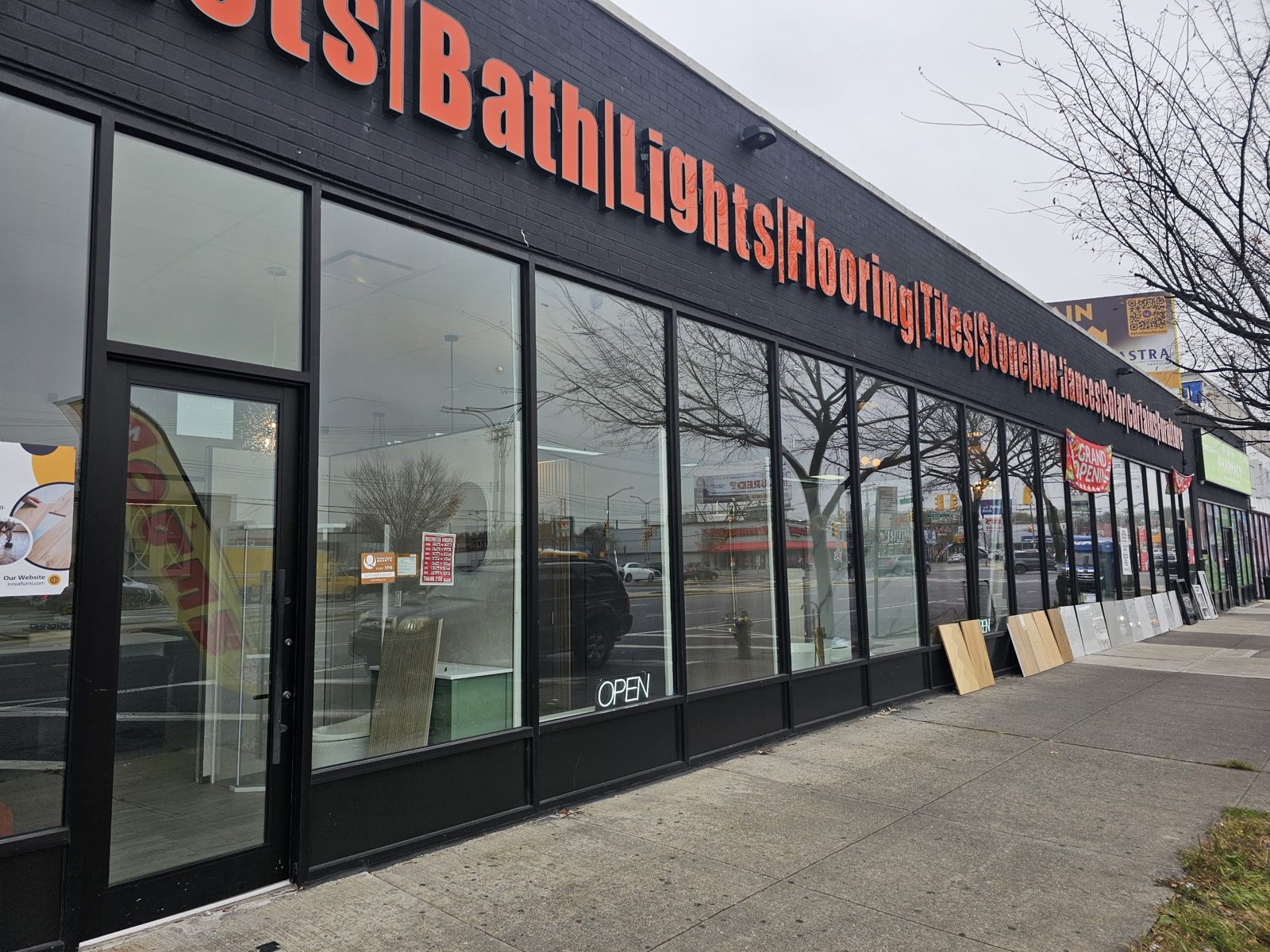 Long run of black aluminium custom storefront with full-height Solarban 60 glass on a low bulkhead at 2461 Flatbush Avenue, Brooklyn, with a full-glass entry door in the foreground