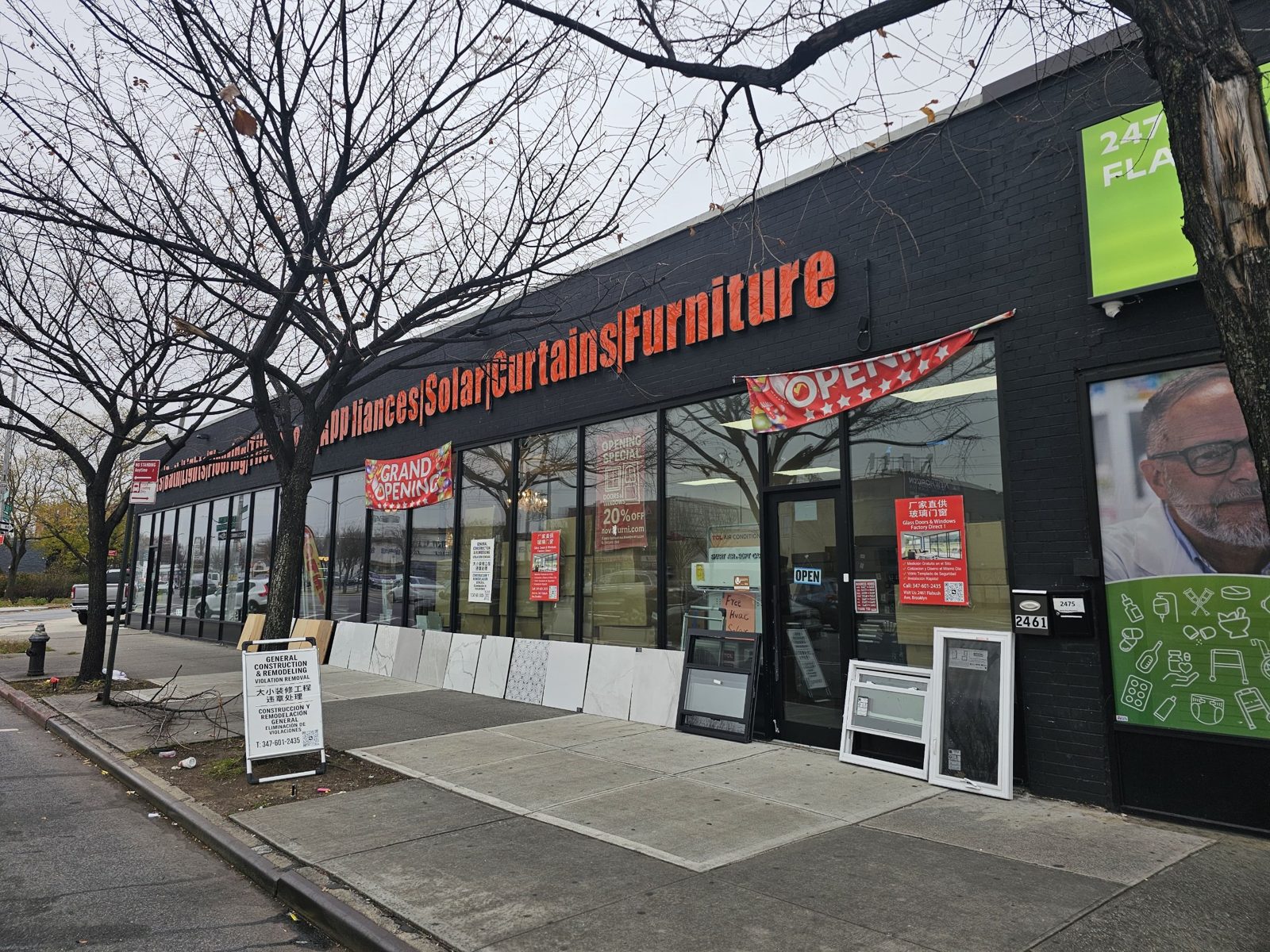 Corner of the black storefront at 2461 Flatbush Avenue near Kings Plaza, Brooklyn, with the entry door, grand-opening banners and building number 2461 on the wall