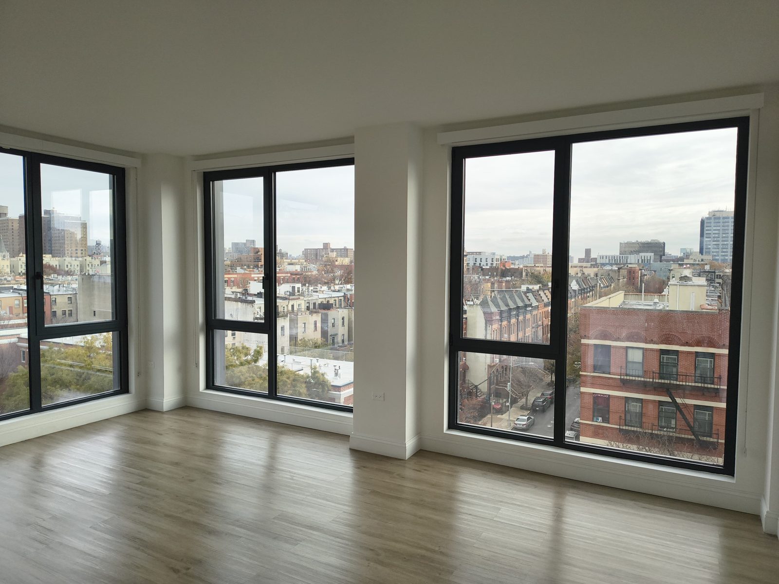 Interior of a corner apartment at 2535 Frederick Douglass Boulevard, Harlem, with oversize black aluminum tilt-and-turn windows on two walls and open views over Manhattan rooftops