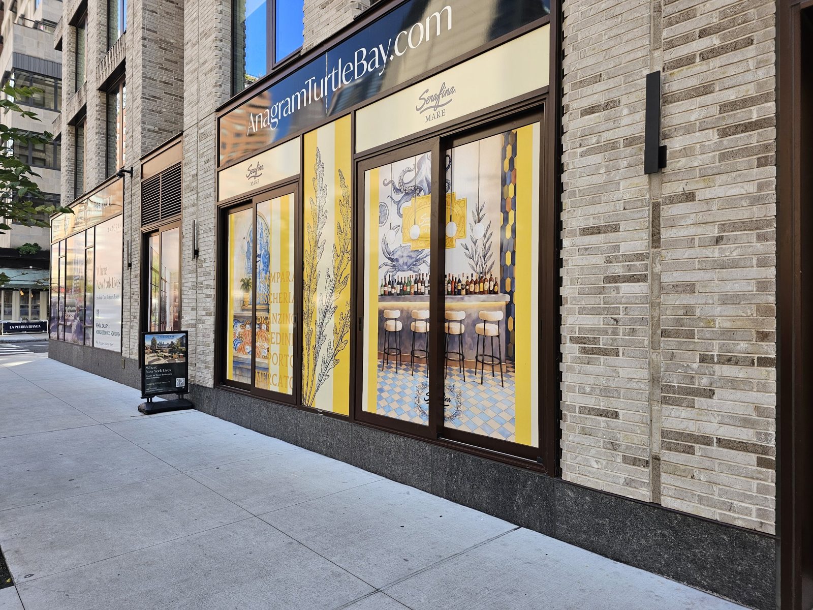 Ground-floor curtain wall at 300 East 50th Street, Manhattan: large glazed bays in dark bronze aluminium between buff brick piers, a leasing sign band above the glass, and an entrance door along the Second Avenue side