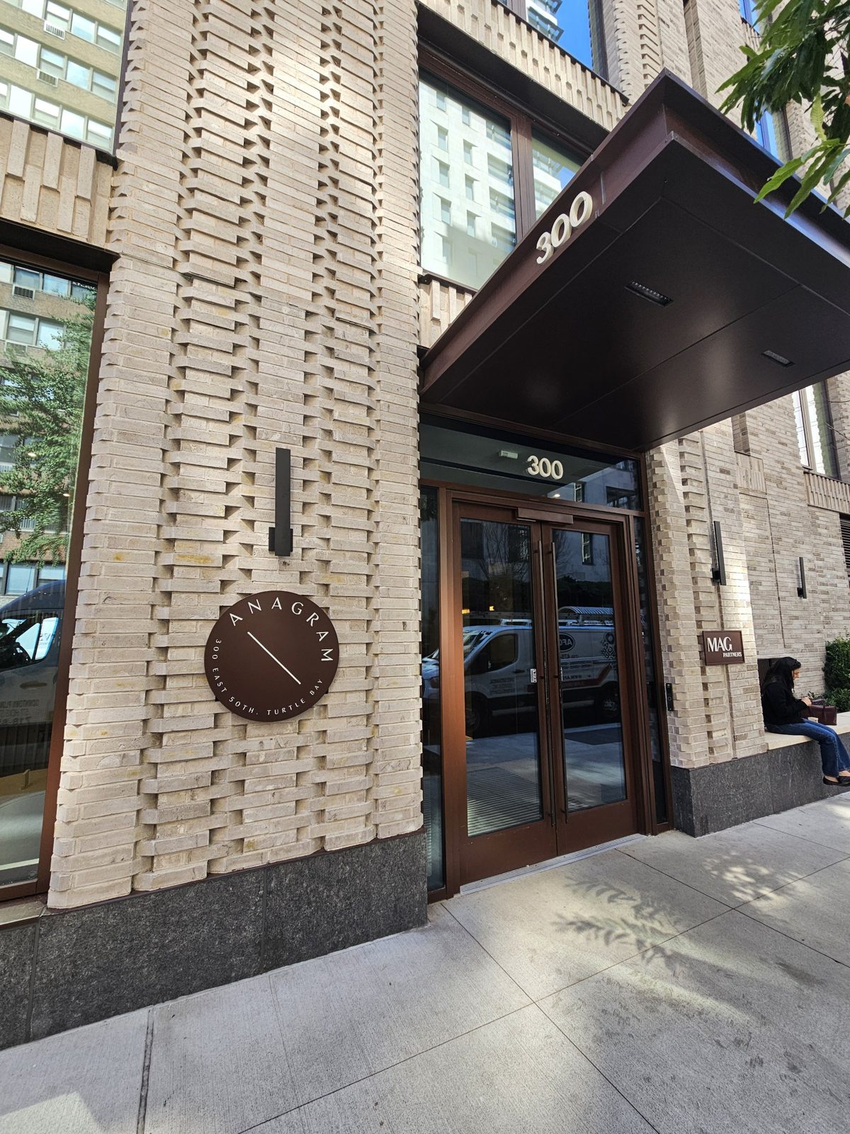 Residential entrance canopy at 300 East 50th Street clad in dark aluminium composite panels, with the building number 300 on the fascia and a pair of full-glass entry doors below