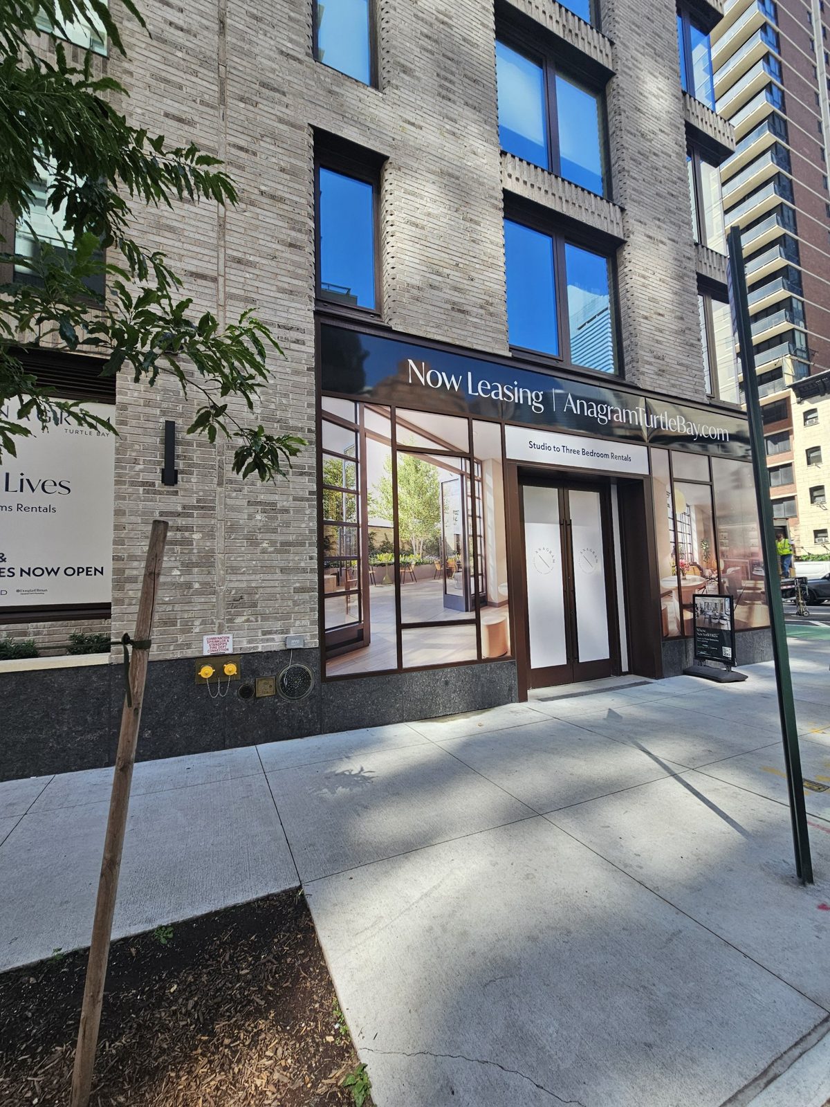 Corner of the ground-floor curtain wall at 300 East 50th Street, Manhattan, showing the leasing entrance double doors, a single door further along, and the sign band over the glazing