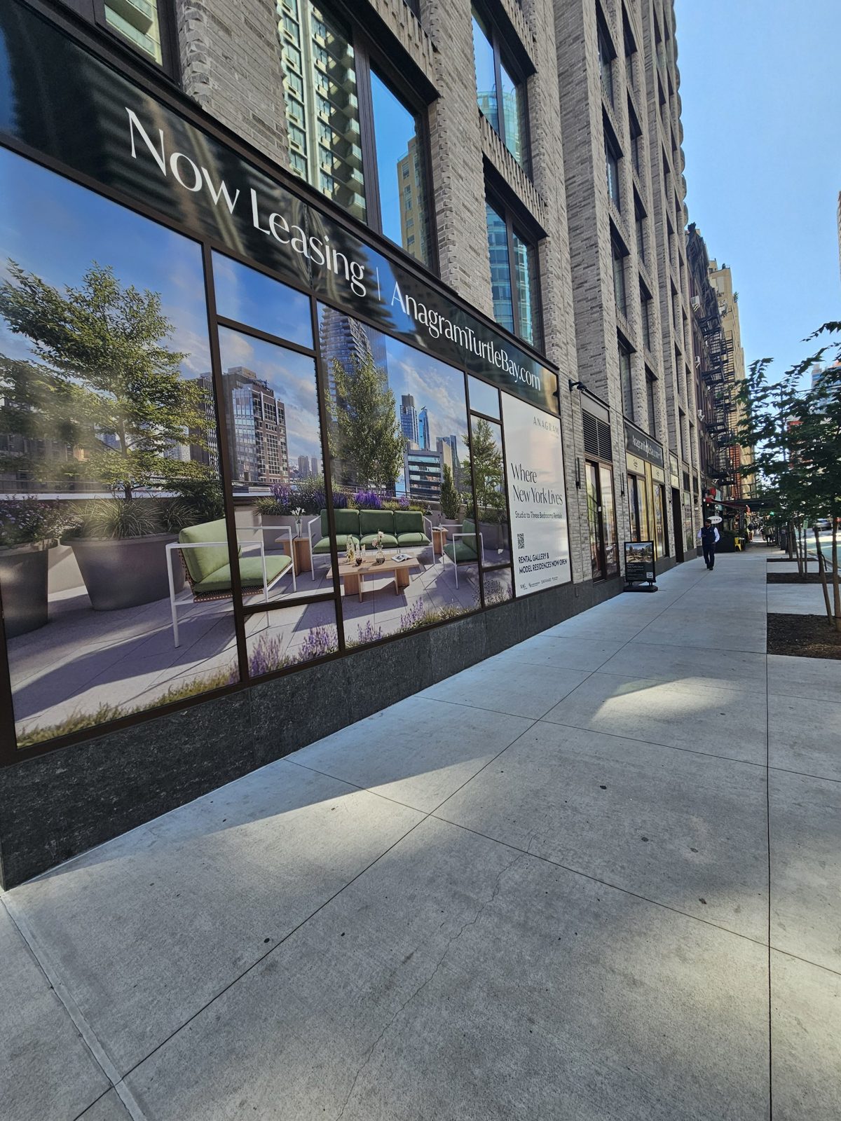 Run of ground-floor curtain wall at 300 East 50th Street, Manhattan, seen along the sidewalk, with the leasing sign band above continuous glazed bays