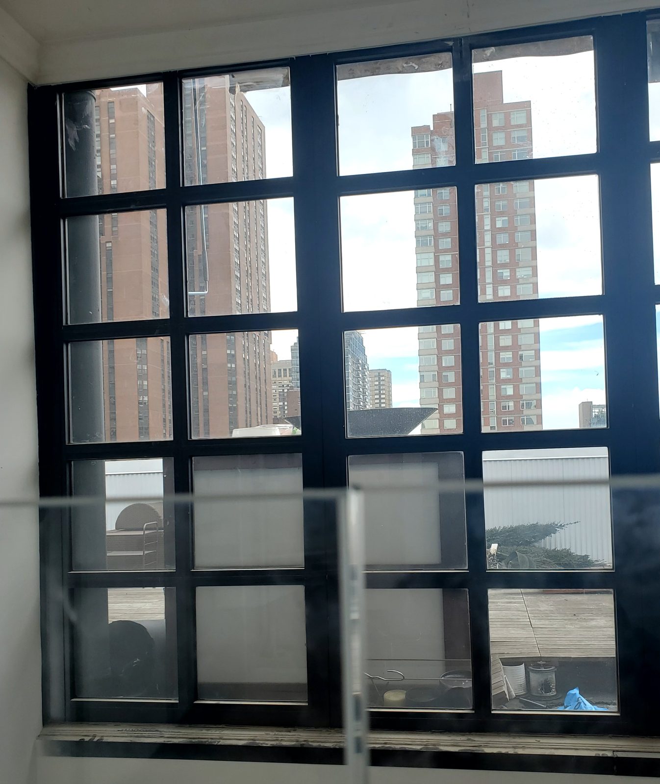Edge of a glass railing panel seen against the black divided-lite window at the 300 East 90th Street penthouse