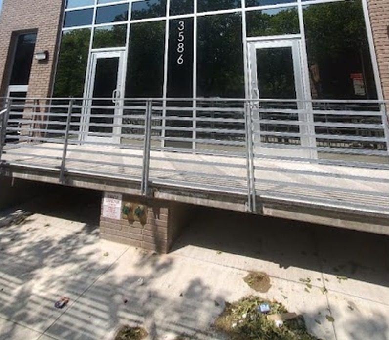 Aluminum entrance doors at the base of the curtain wall, behind the landing railing, at 3586 Nostrand Avenue, Brooklyn