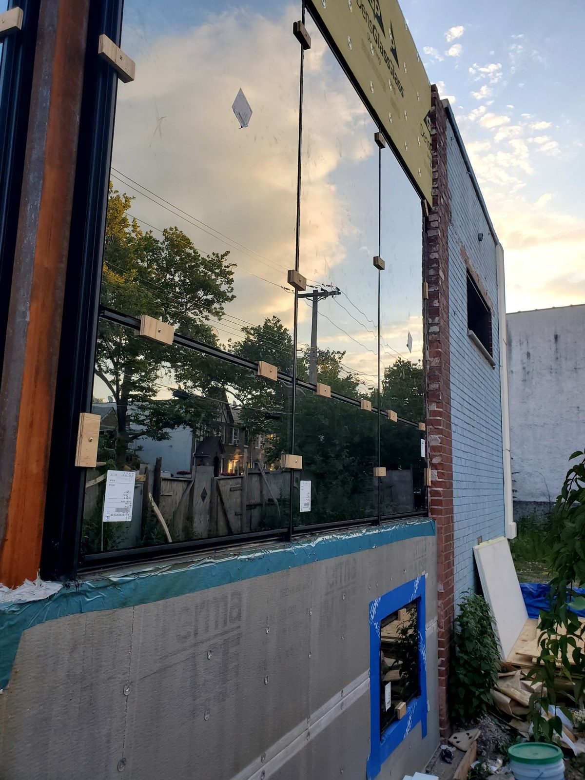 Corner curtain wall glass held with temporary wood blocks during installation at 3915 Flatlands Avenue, Brooklyn