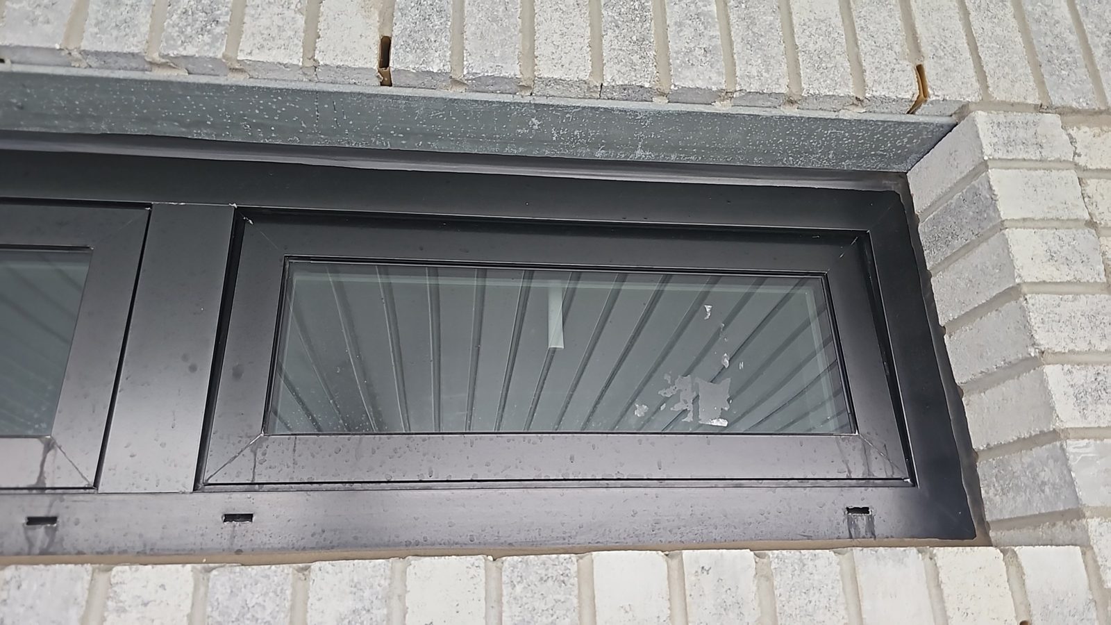 Black aluminum Alutech hopper window in a light brick wall at 5101 Beach 51st Street, Sea Gate, Brooklyn, with weep slots in the frame