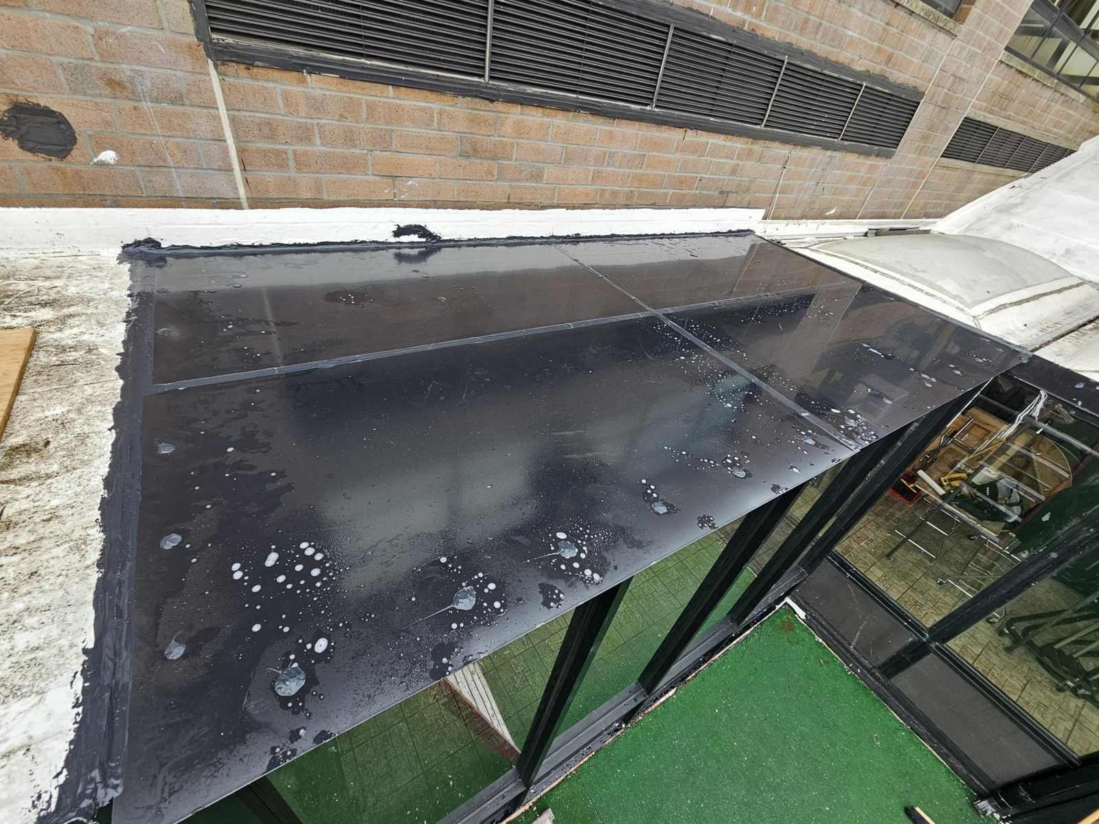 Flat black panel roof of the enclosure at 590 Bedford Avenue, Brooklyn, sealed to the brick wall and flashed to the deck parapet
