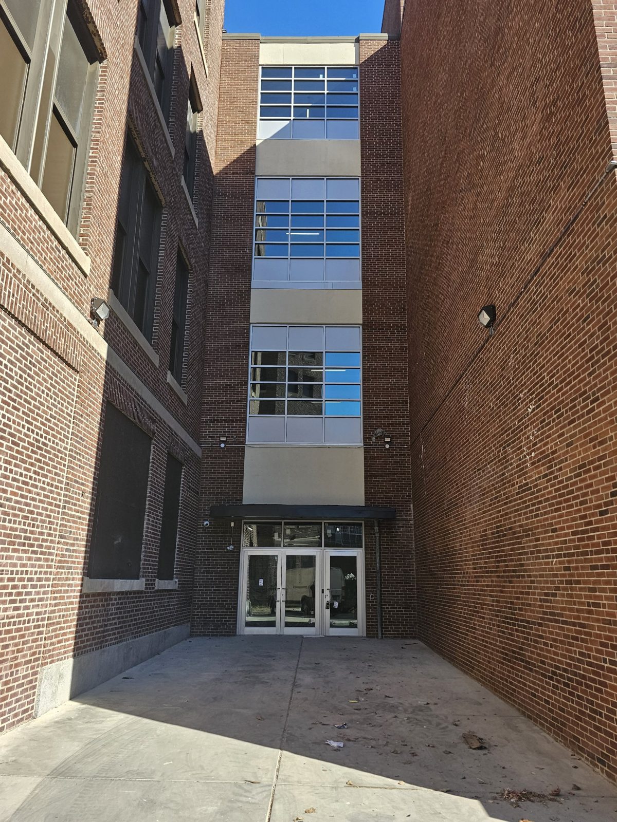 Stack of clear anodized aluminium window-wall bays with fixed glass and solid panels on the stair tower between two brick wings of the former Germantown High School building at 60 East Haines Street, Philadelphia