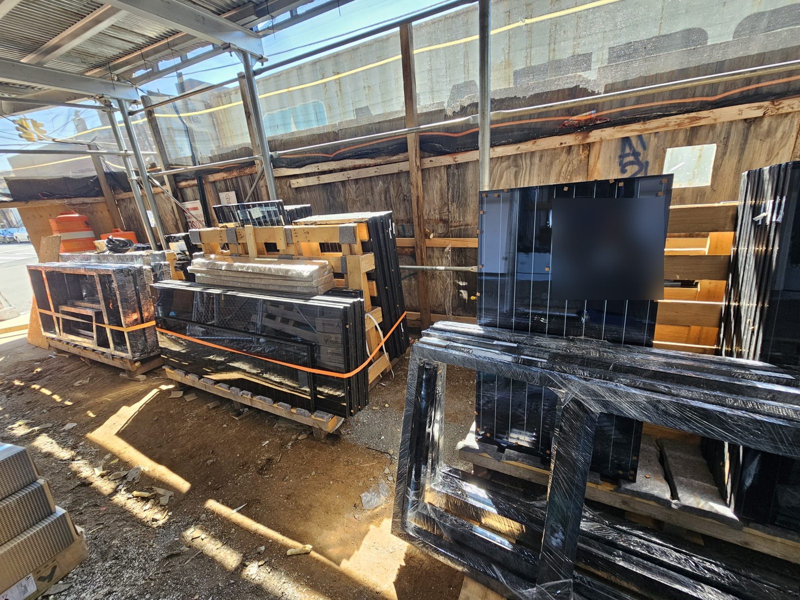 Black aluminum window frames and insulating glass units delivered on pallets and staged under the sidewalk shed at 61 Avenue U, Brooklyn, before installation