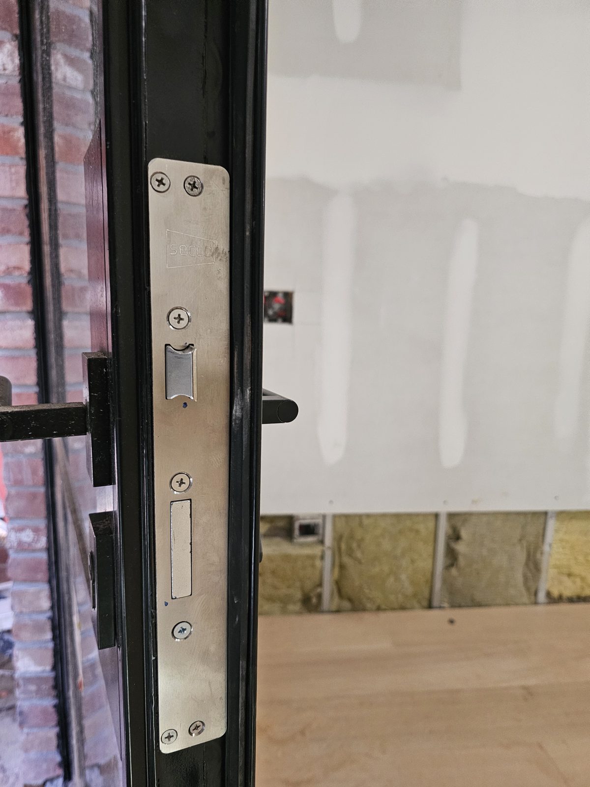 Stainless lock keeper set into the black frame of a SIMPAS in-swing door