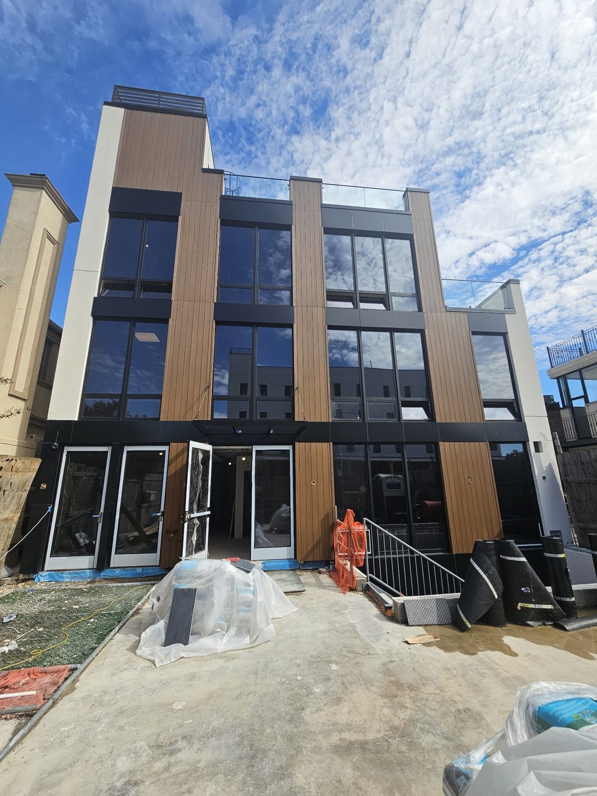 Rear elevation of a new residential building at 75-65 186th Street, Fresh Meadows, Queens, with black ACM spandrel panels, wood-look rigid panels and a black aluminum entrance canopy