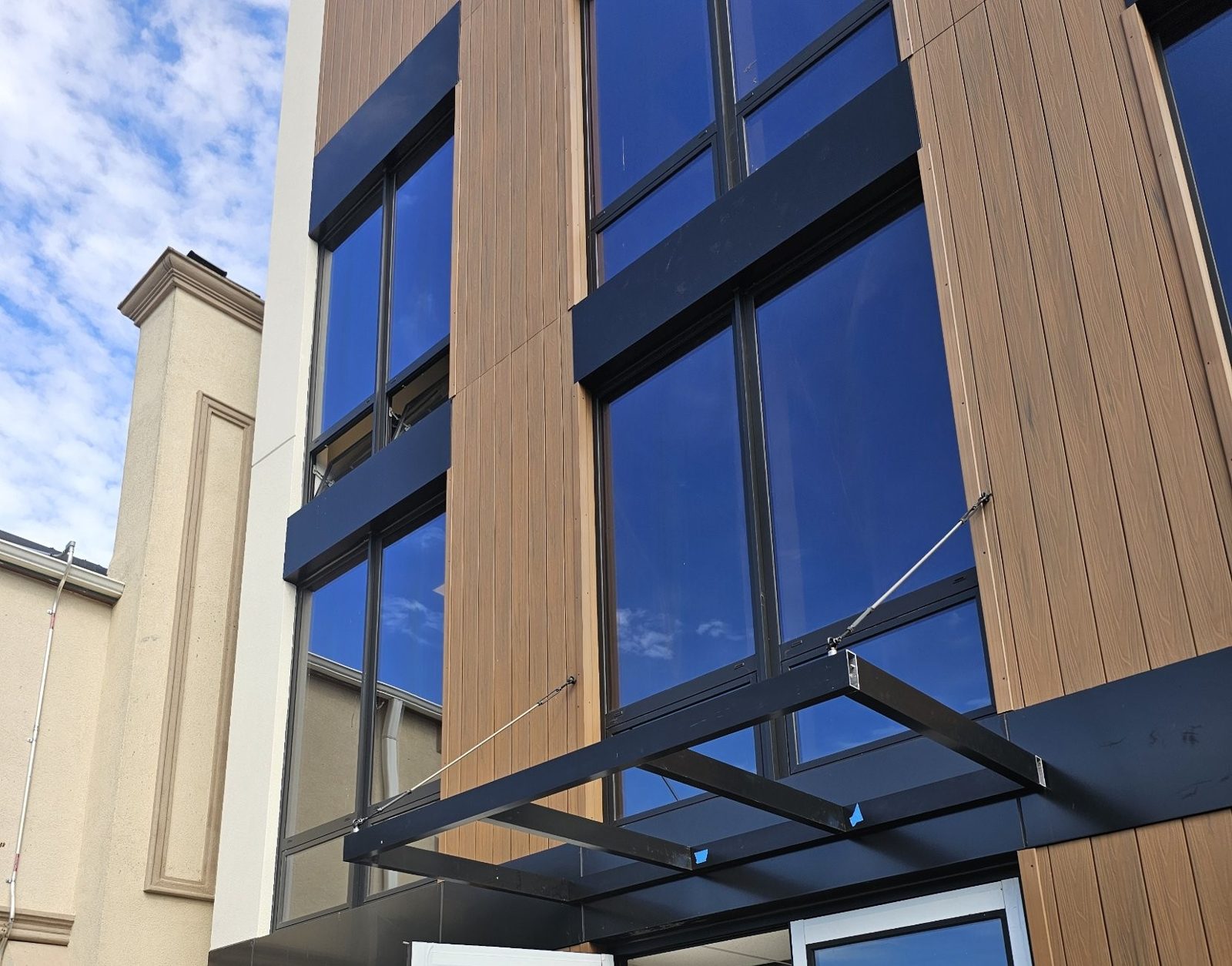 Black aluminum entrance canopy on cable stays over the entrance doors at 75-65 186th Street, Queens