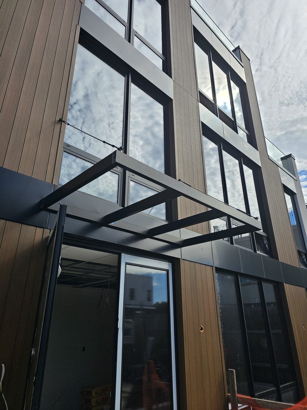 Underside of the black aluminum canopy frame of box sections at 75-65 186th Street, Queens, with cable stays to the facade above