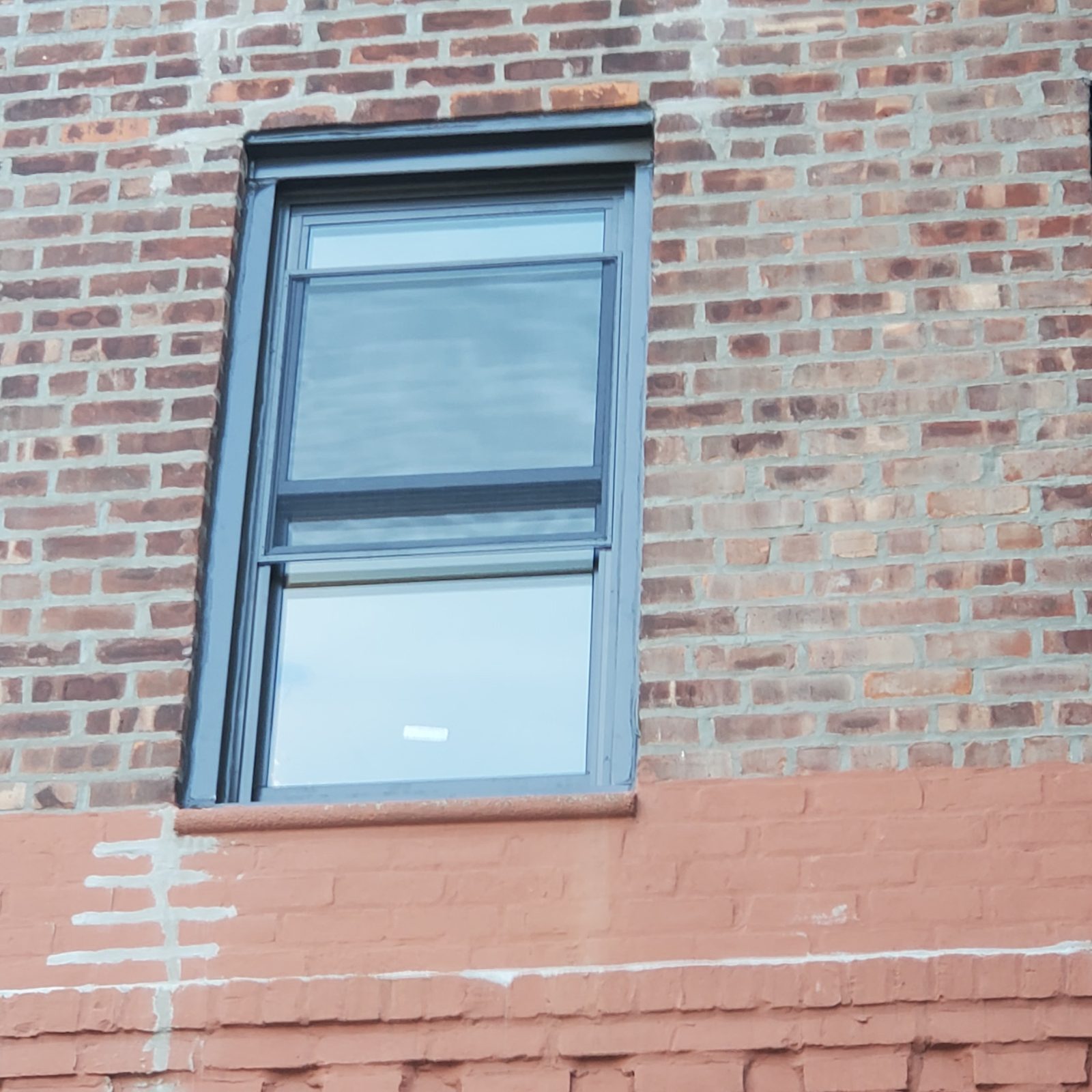 Single dark-framed double-hung replacement window with insect screen in a brick wall, Brighton Beach, Brooklyn