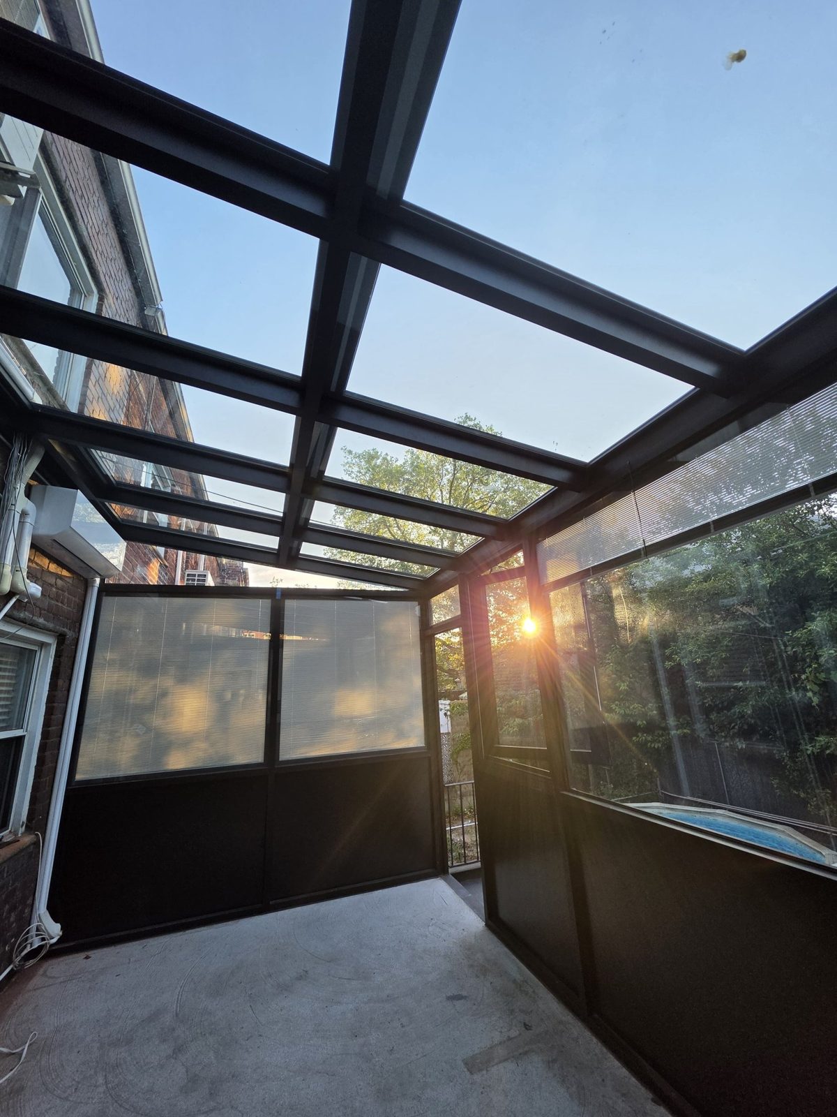 Interior of a black aluminum sunroom looking up through the glass roof at sunset, Brooklyn, NY