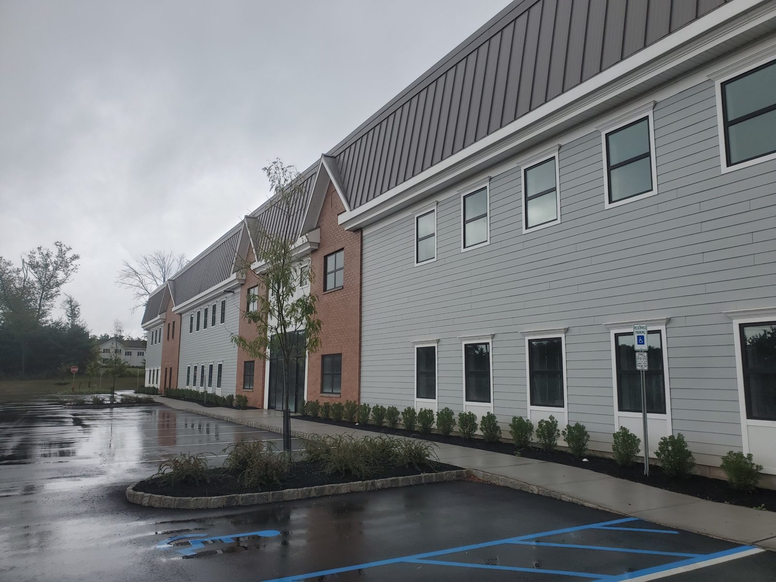 New warehouse in Central New Jersey with a facade of siding, brick and gables designed to blend with neighboring homes, with dark aluminum windows