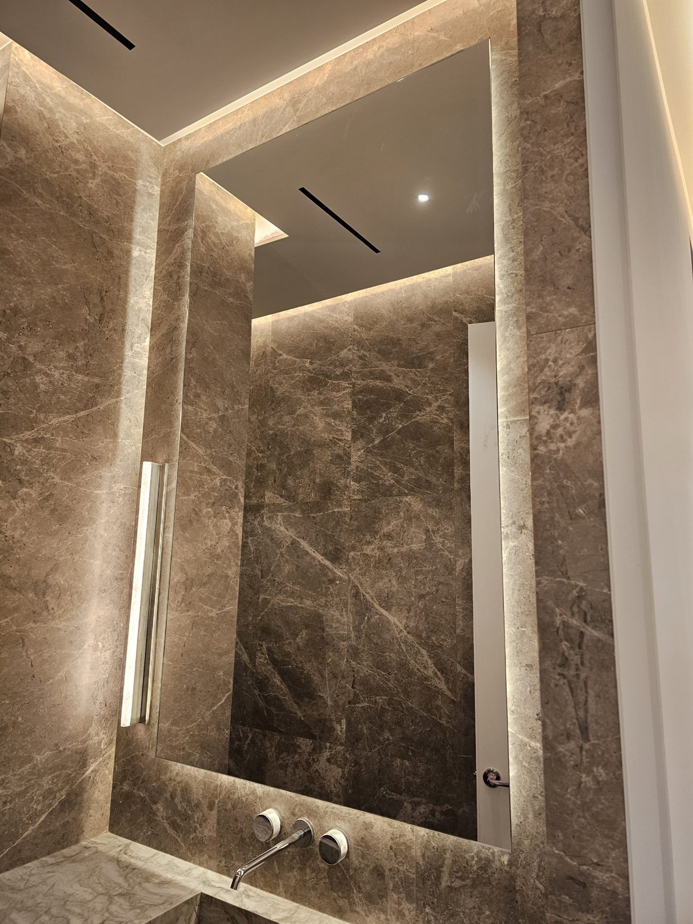 Full-height low-iron LED backlit mirror on brown veined marble with a wall-mounted spout and a vertical light bar, East 18th Street apartment, Manhattan