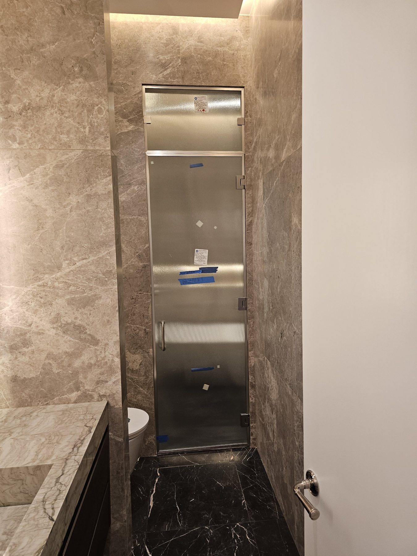 Custom textured obscure-glass shower door with a pivoting ventilation window above, brushed-nickel frame, in a narrow marble shower stall, East 18th Street, Manhattan