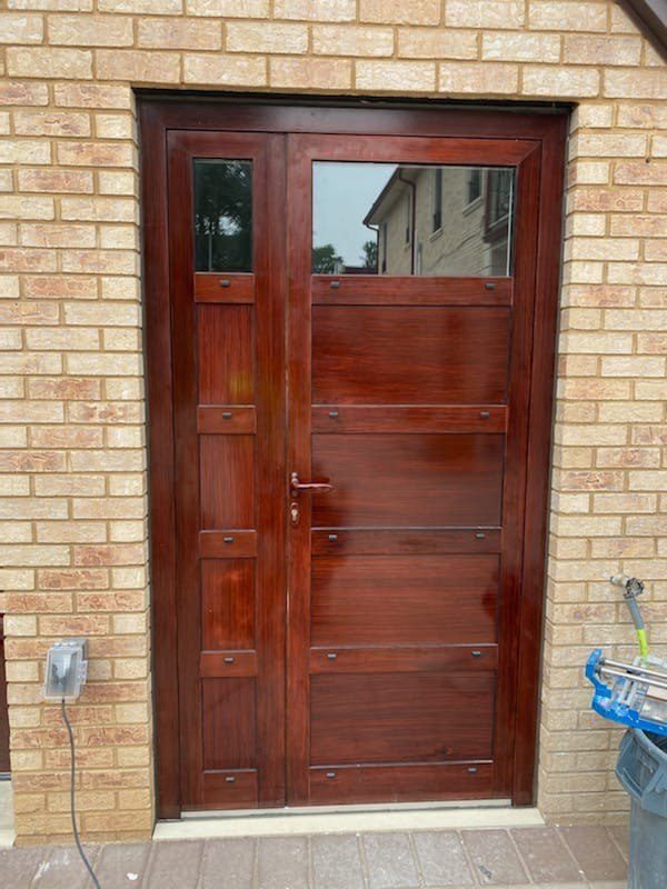 Paneled garage entry door with sidelite in a custom red-brown patina paint finish, set in pale brick at a private house in Jamaica Estates, Queens