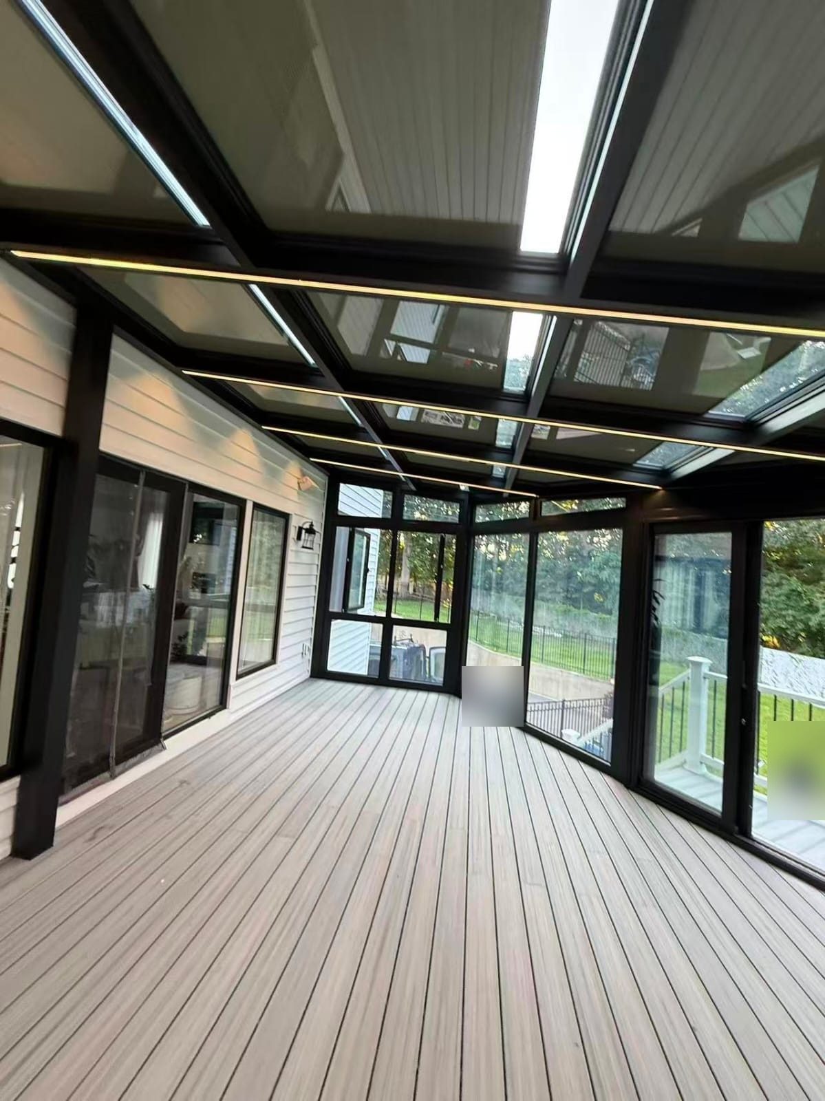 Interior of the custom sunroom in Manalapan, NJ, showing the glass roof on black rafters with light strips and floor-to-ceiling glass walls