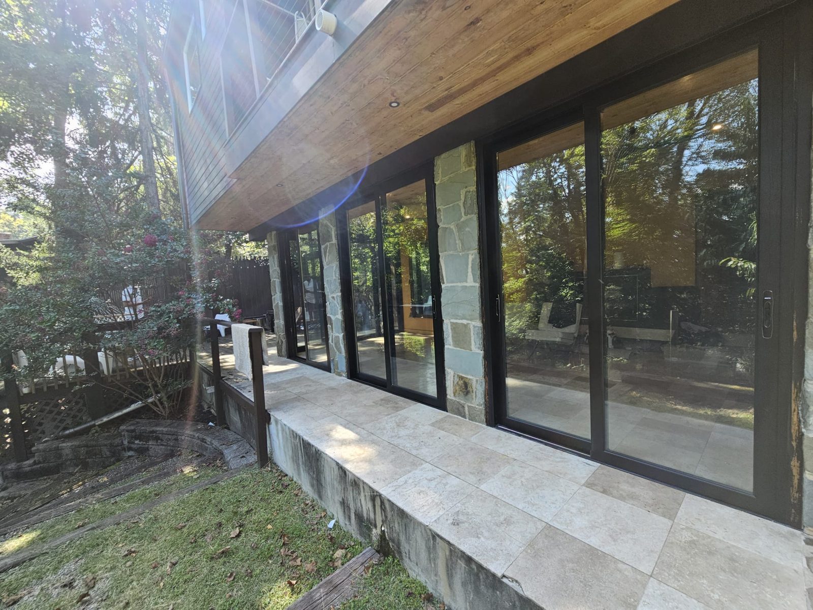 Run of black aluminium sliding doors between fieldstone piers along a travertine terrace, sunroom near Morristown NJ