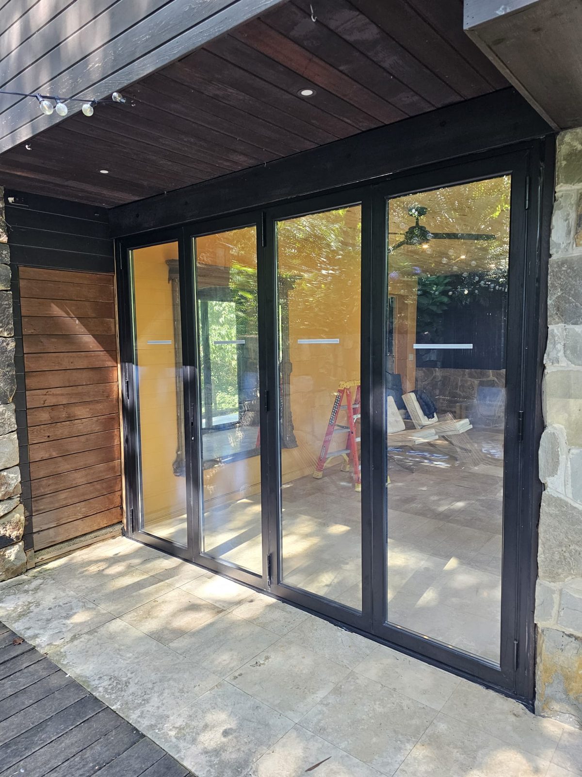 Four-panel black aluminium bifold door under a dark wood overhang, opening the sunroom to a deck, near Morristown NJ