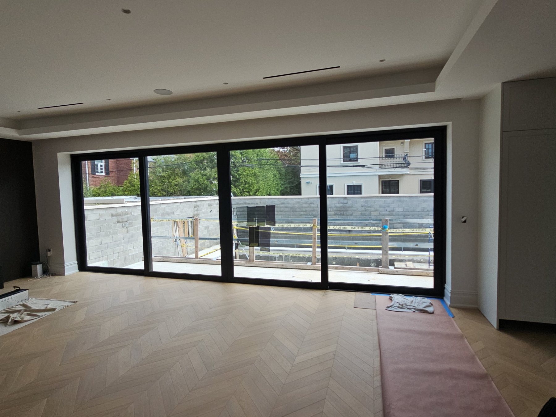 Four-panel black aluminum sliding door wall opening onto a terrace, seen from inside a new house with a herringbone oak floor, Ocean Avenue, Brooklyn