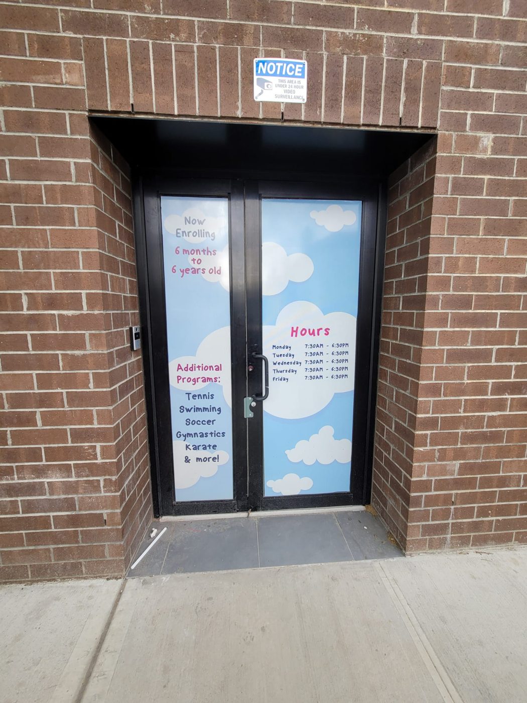 Black aluminum commercial entrance with an unequal pair of doors: a wide master leaf with the pull and lock, and a narrow inactive leaf opened only for deliveries