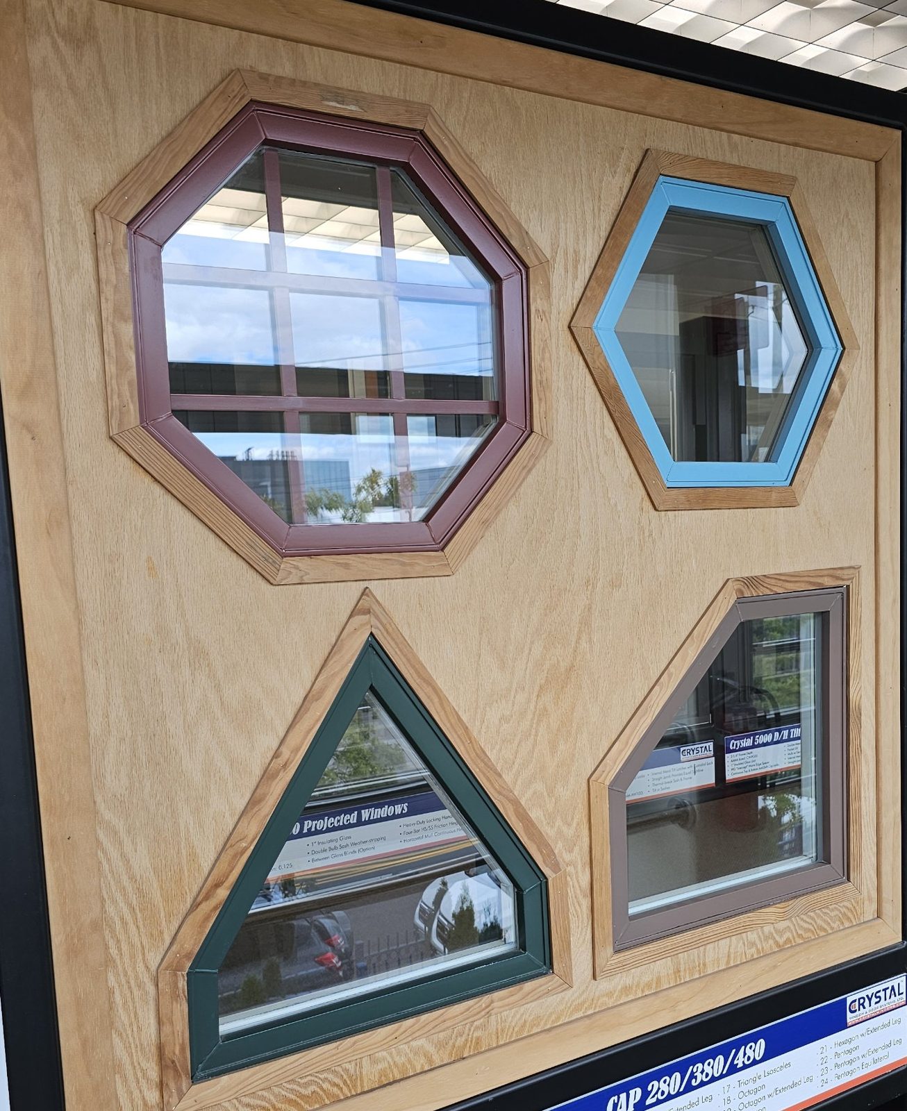 Crystal architectural shape window samples on a showroom display: an octagon with grids in burgundy, a hexagon in light blue, a triangle in dark green and a trapezoid in brown