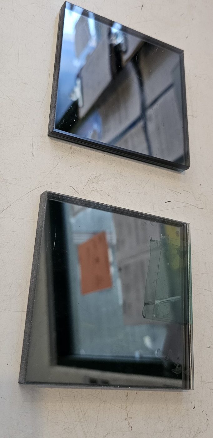 Two laminated smoke mirror samples: a smoke mirror laminated to clear glass above, and a smoke mirror laminated to a second mirror below