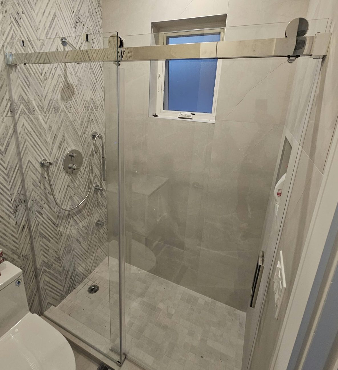 Frameless single sliding shower door with a fixed glass panel, a sliding door on two rollers and a polished header bar