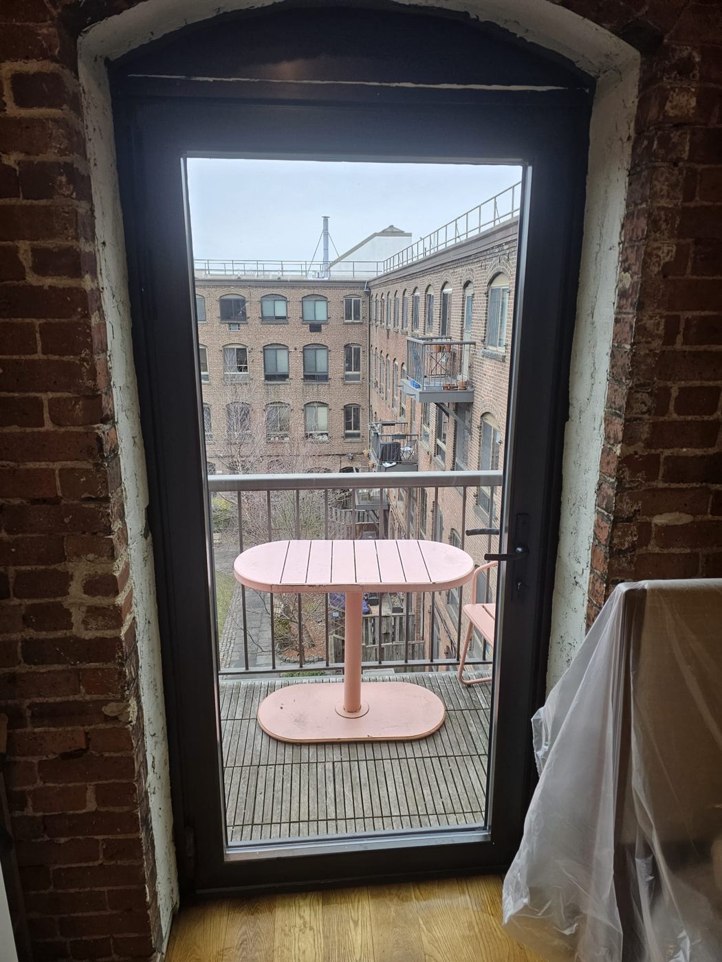 Single-leaf dark aluminum terrace door with full-height glass and a lever handle, set in an arched brick opening and leading to a balcony