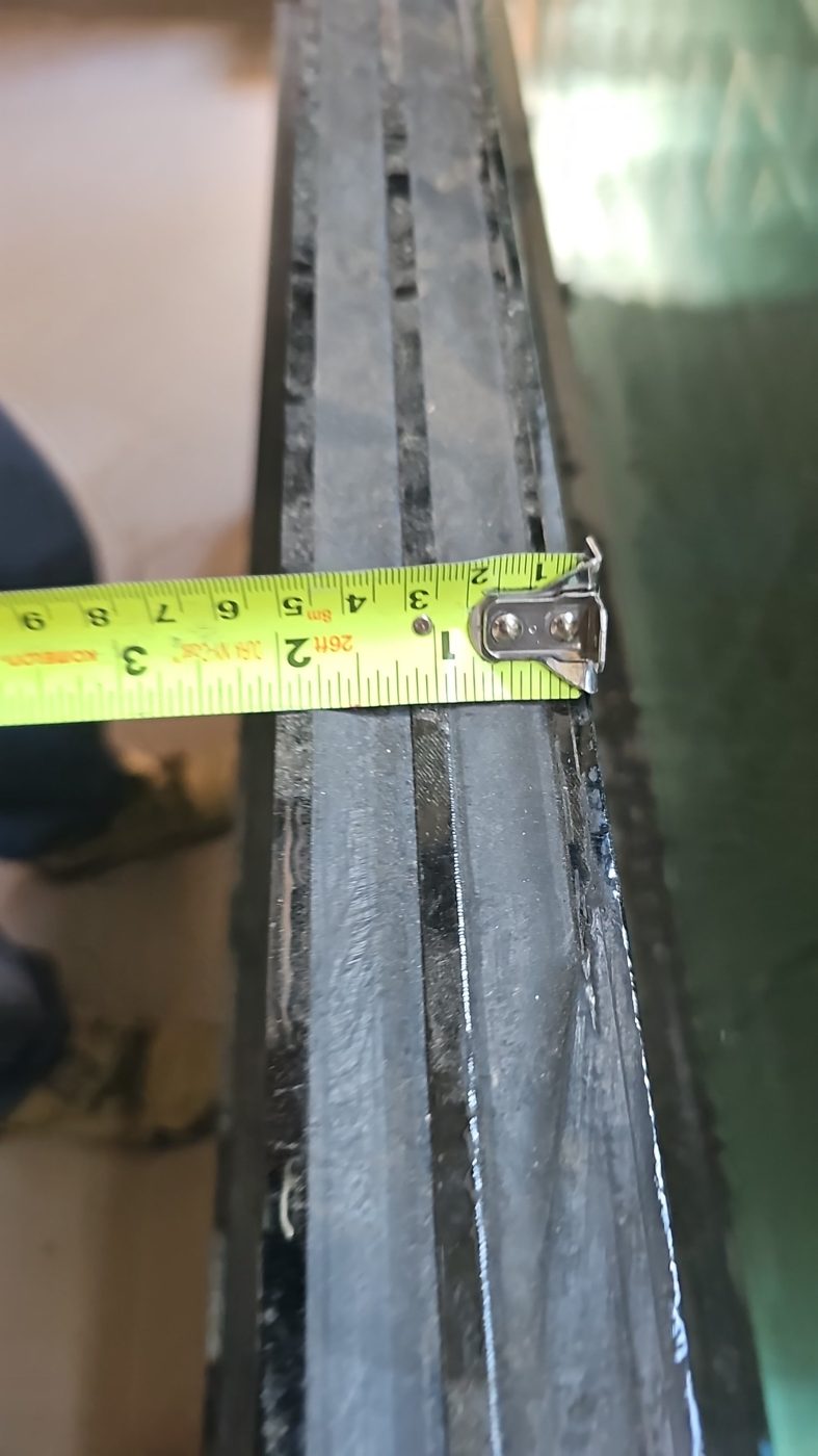 Edge of a triple insulating glass unit sample with a tape measure across it, showing three lites of glass, two black spacer cavities and an overall thickness of about 2 inches